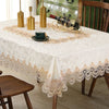A white embroidered lace tablecloth is set on a wooden table with gold-colored decanters and a bottle.
