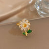 A gold cocktail ring featuring a flower design with clear stones and an attached green leaf.