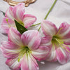 Three pink and white artificial lilies with buds displayed on a white cloth.
