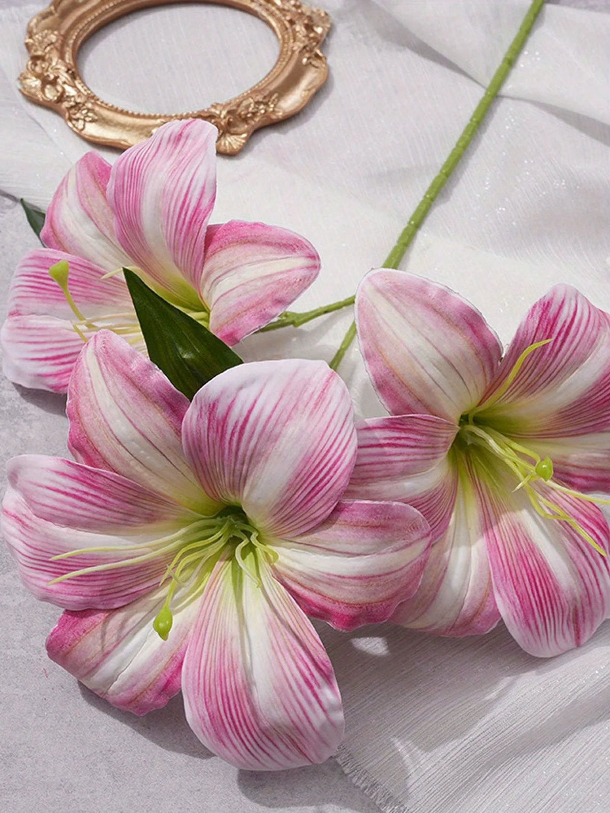 Three pink and white artificial lilies with buds displayed on a white cloth.