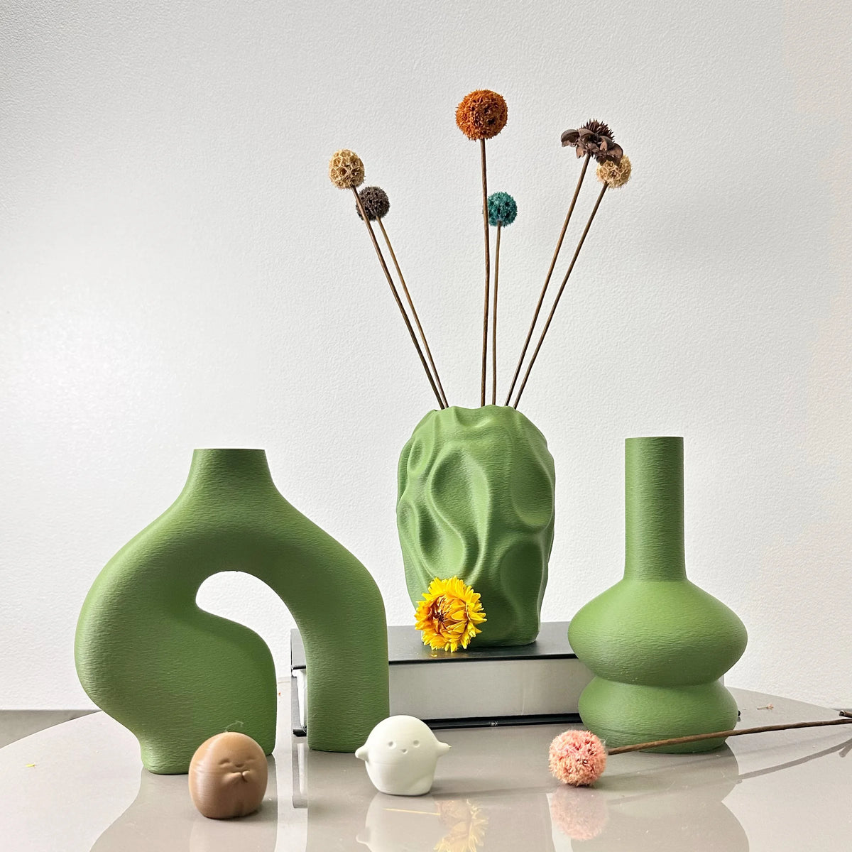 A set of three geometric ceramic vases in various shades of green and brown with dried floral elements.
