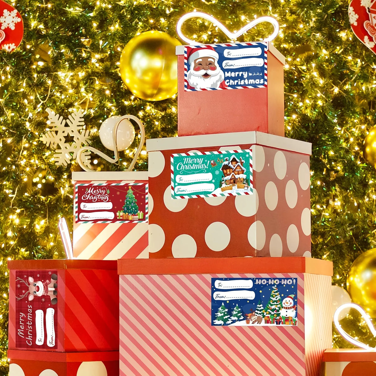 A stack of red and white Christmas gift boxes decorated with festive tags and wrapped in sparkling green tinsel.