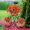 A display of bright orange and red artificial flowers in wooden planters mounted on a black metal stand, set against green fo