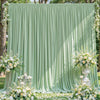 A soft sage green fabric backdrop with vertical pleats decorated with white floral arrangements.