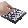 A hand is placing white chess pieces onto a black and white checkered board of a portable folding magnetic chess set.