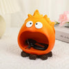 An orange resin fire spirit figurine with large eyes and an open mouth, resting on a white cloth.