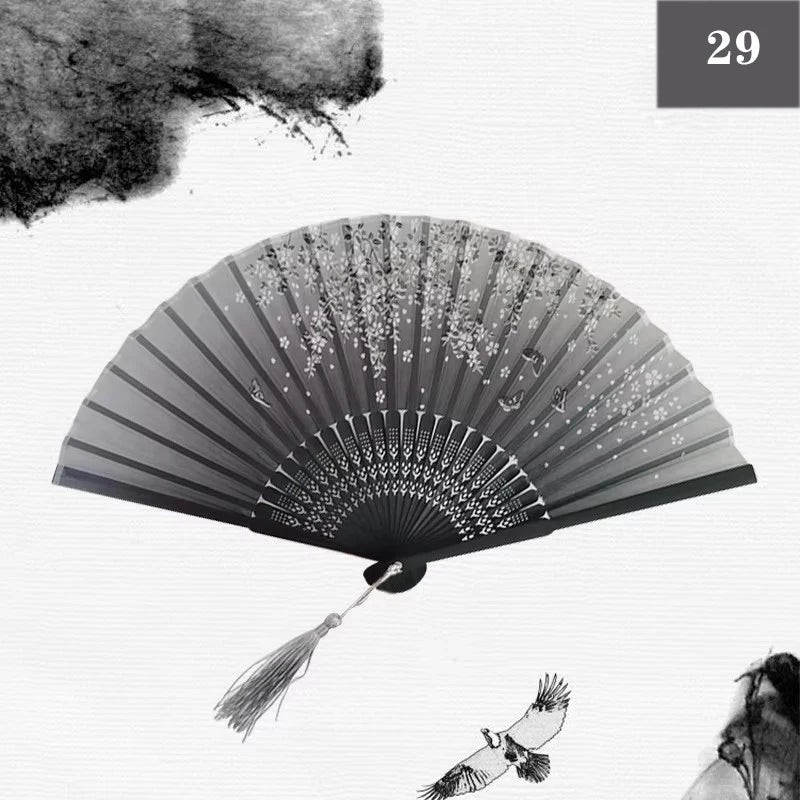 A black and white photograph of a vintage silk bamboo folding hand fan with delicate floral designs.
