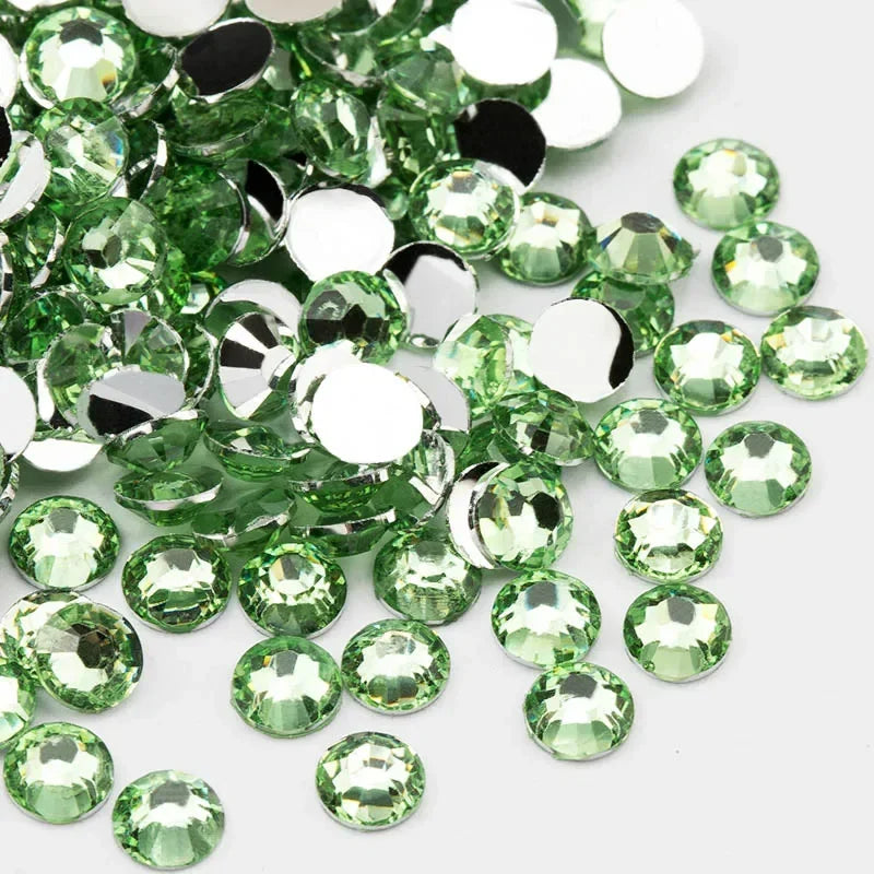 A scattered pile of round flatback resin rhinestones in various shades of green and clear white.