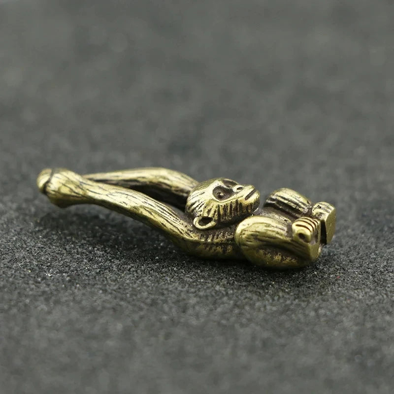 Vintage brass monkey key chain charm lying on a dark gray surface.