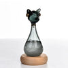 A glass bottle decoration shaped like an Egyptian cat with a green body and gold accents, resting on a wooden base.