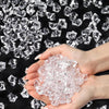 A hand holds crushed clear acrylic pebbles against a background of larger diamond-shaped crystals.