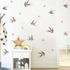 Weiße Wand mit abnehmbaren Vogel- und Stern-Aufklebern und einem Holzregal darunter.