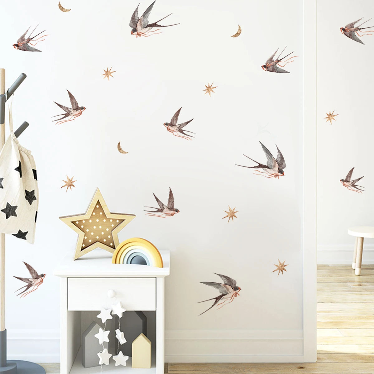Weiße Wand mit abnehmbaren Vogel- und Stern-Aufklebern und einem Holzregal darunter.