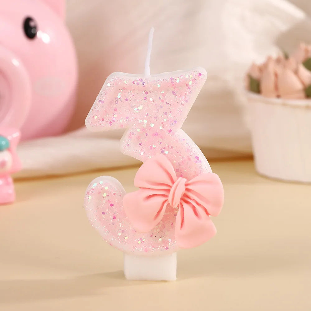 A pink glitter birthday candle shaped like the number three with a bow, set against a light background.