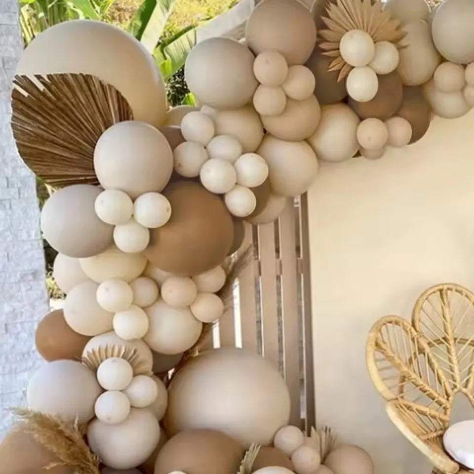 A decorative balloon garland featuring various shades of beige, cream, and brown balloons arranged on a white wall.