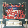 A motivational tapestry wall hanging featuring the text Get Out of Your Head displayed above a bed.