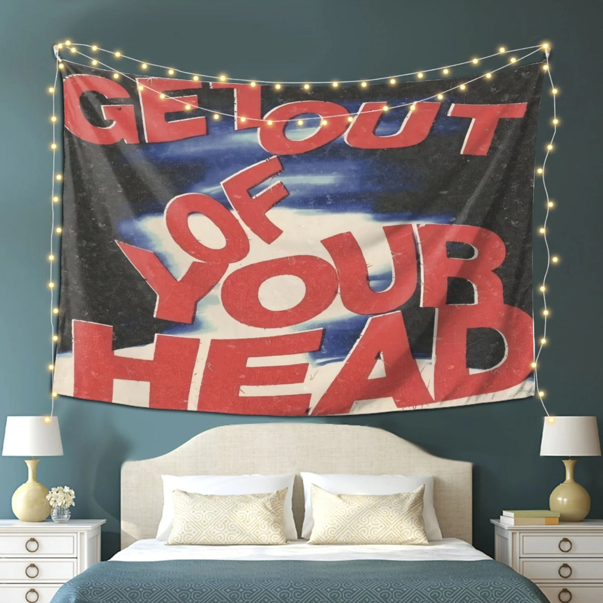 A motivational tapestry wall hanging featuring the text Get Out of Your Head displayed above a bed.