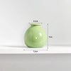 A light green ceramic mini vase with a rounded body and narrow neck, shown on a white shelf.