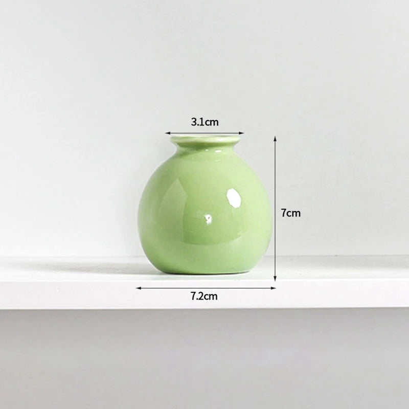 A light green ceramic mini vase with a rounded body and narrow neck, shown on a white shelf.
