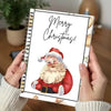 A hand holds a spiral-bound Christmas card booklet featuring a festive Santa Claus illustration and Merry Christmas text.