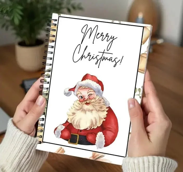 A hand holds a spiral-bound Christmas card booklet featuring a festive Santa Claus illustration and Merry Christmas text.