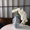 A hand-painted blue and white porcelain vase holds a cluster of white orchids against a light gray background.