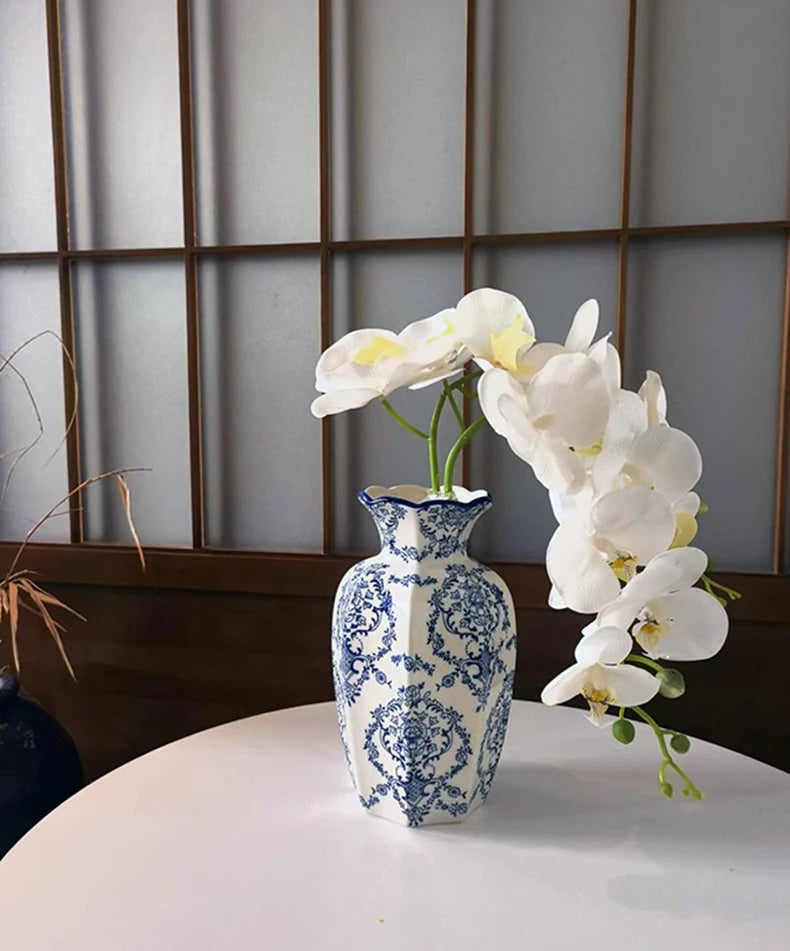 A hand-painted blue and white porcelain vase holds a cluster of white orchids against a light gray background.