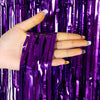 A hand is holding purple metallic foil fringe curtain backdrop fabric.