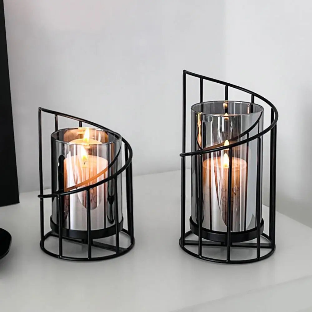 A black metal candle holder with a glass cylinder and a candle inside, displayed on a white surface.