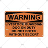 An orange metal warning sign with black text that reads WARNING LIVESTOCK GUARDIAN DOG ON DUTY DO NOT ENTER WITHOUT ESCORT