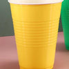 A bright yellow disposable party cup is shown standing on a pink surface.