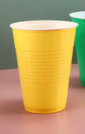 A bright yellow disposable party cup is shown standing on a pink surface.