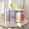 A set of three modern decorative fake books featuring yellow flowers and pink covers with Japanese text.