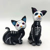 A resin figurine set featuring a black cat and a white cat with colorful markings, depicting Day of the Dead themes.