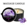 A black jar candle labeled Massage Candle Lavender with a lit wick and purple lavender flowers nearby.