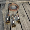 A rustic wreath of twigs with hanging brass bells and leather cords on a weathered wooden surface.