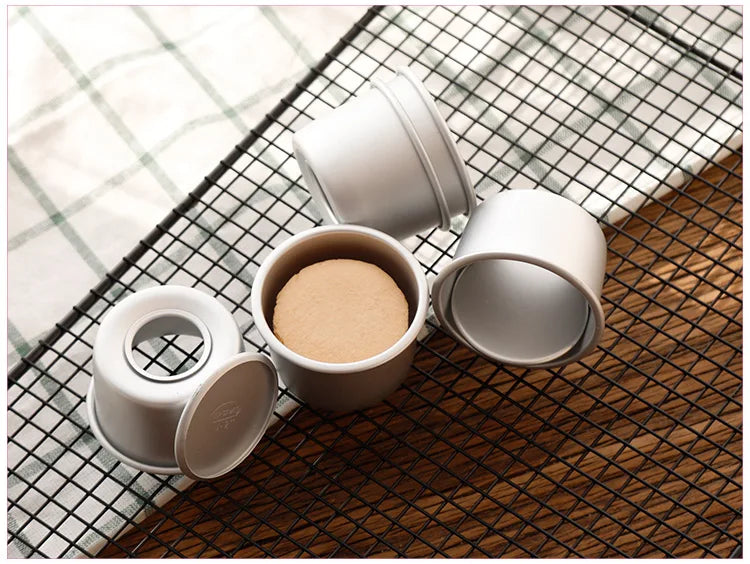 A set of five white non-stick round cake molds with removable bases resting on a dark wooden surface and a checkered cloth.
