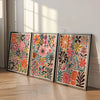 Un set de tres lienzos de arte floral botánico enmarcados con flores y follaje coloridos.