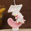 Una vela blanca con forma de número 3, purpurina rosa y una pequeña figura de unicornio en la base.