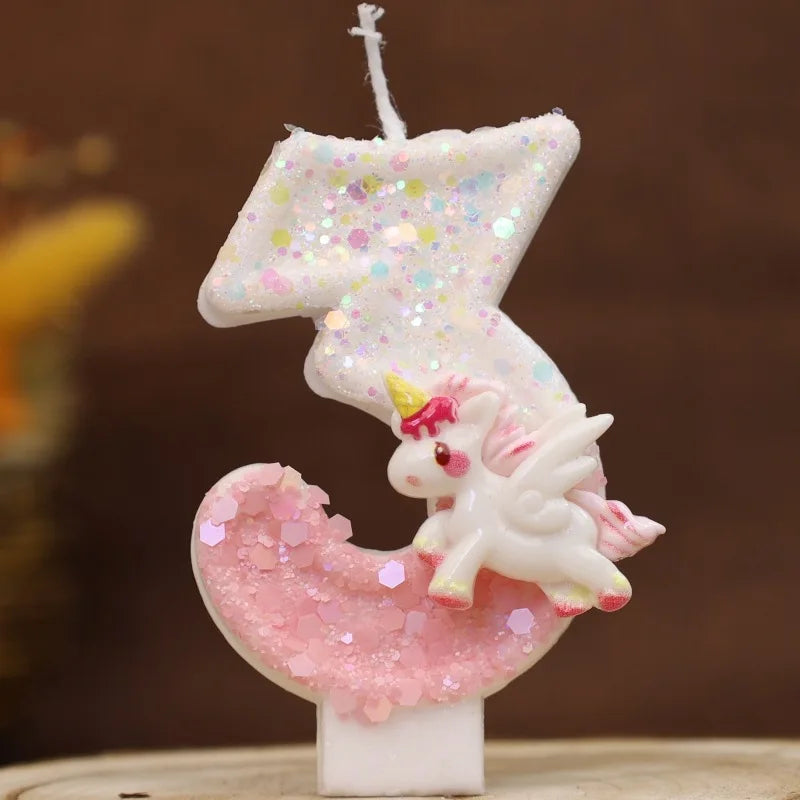 Una vela blanca con forma de número 3, purpurina rosa y una pequeña figura de unicornio en la base.