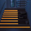 A modern staircase illuminated by warm orange LED strips, highlighting the steps and a window view.
