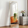 A full-length arched floor mirror with a gold aluminum frame leaning against a white wall.