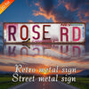 Vintage Retro Metall-Straßenschild für Rose Rd in rot-pinkem Ton vor einem Sonnenuntergangshimmel.