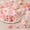 A collection of pink and peach silk artificial flower heads for crafts and decor arranged on a light background.