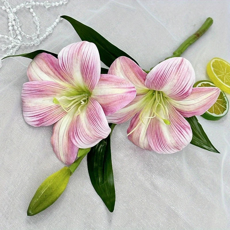 Three pink and white artificial lilies with green buds displayed on a light fabric.