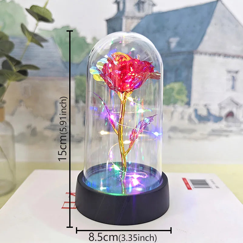 A glass dome containing a vibrant pink rose with an LED light, displayed on a white surface.