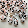 A collection of handmade crochet cow keychains in white and black with pink accents.