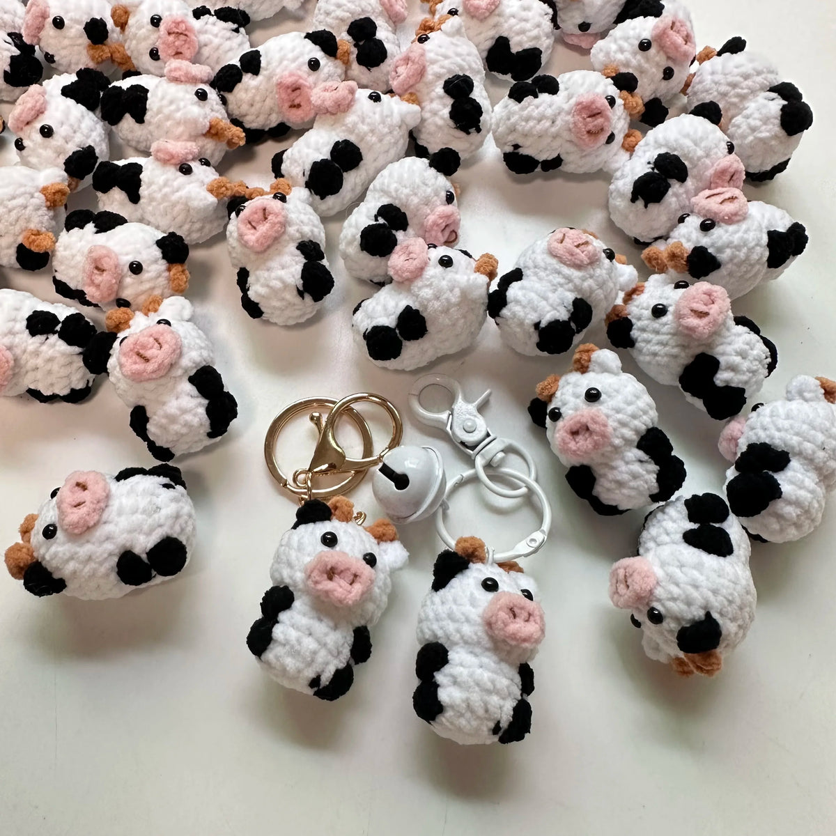 A collection of handmade crochet cow keychains in white and black with pink accents.