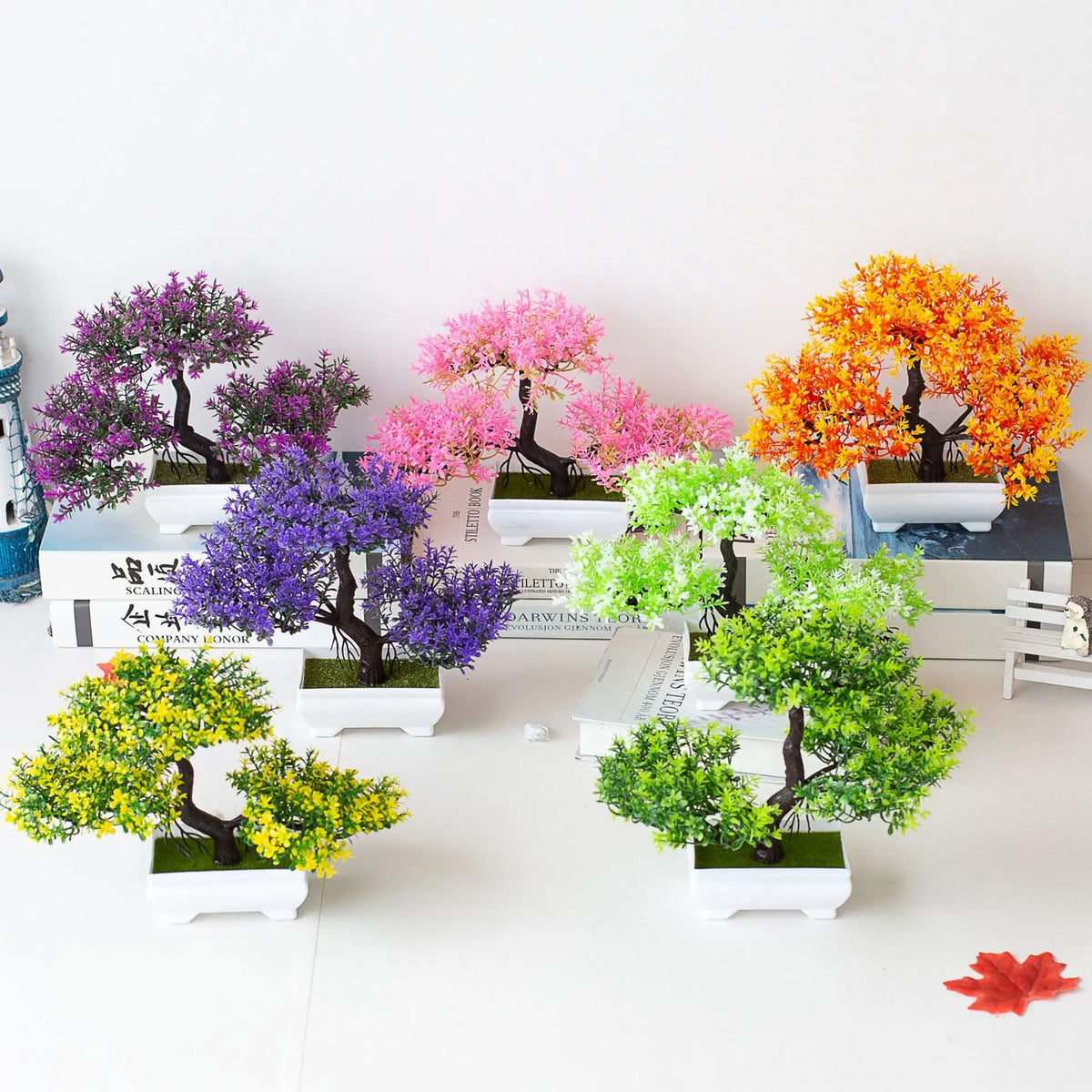 A collection of artificial tree bonsai decorations in various shades of purple, pink, and orange displayed on a white surface
