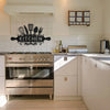 A rustic farmhouse metal wall sign featuring silhouette utensils mounted above a stainless steel oven in a kitchen.